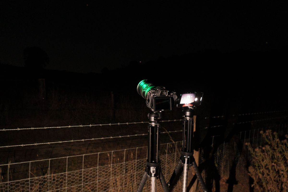 Pixel phone and Nikon mirrorless camera side by side mounted to tripods at night, with the astrophotography mode active on the Pixel