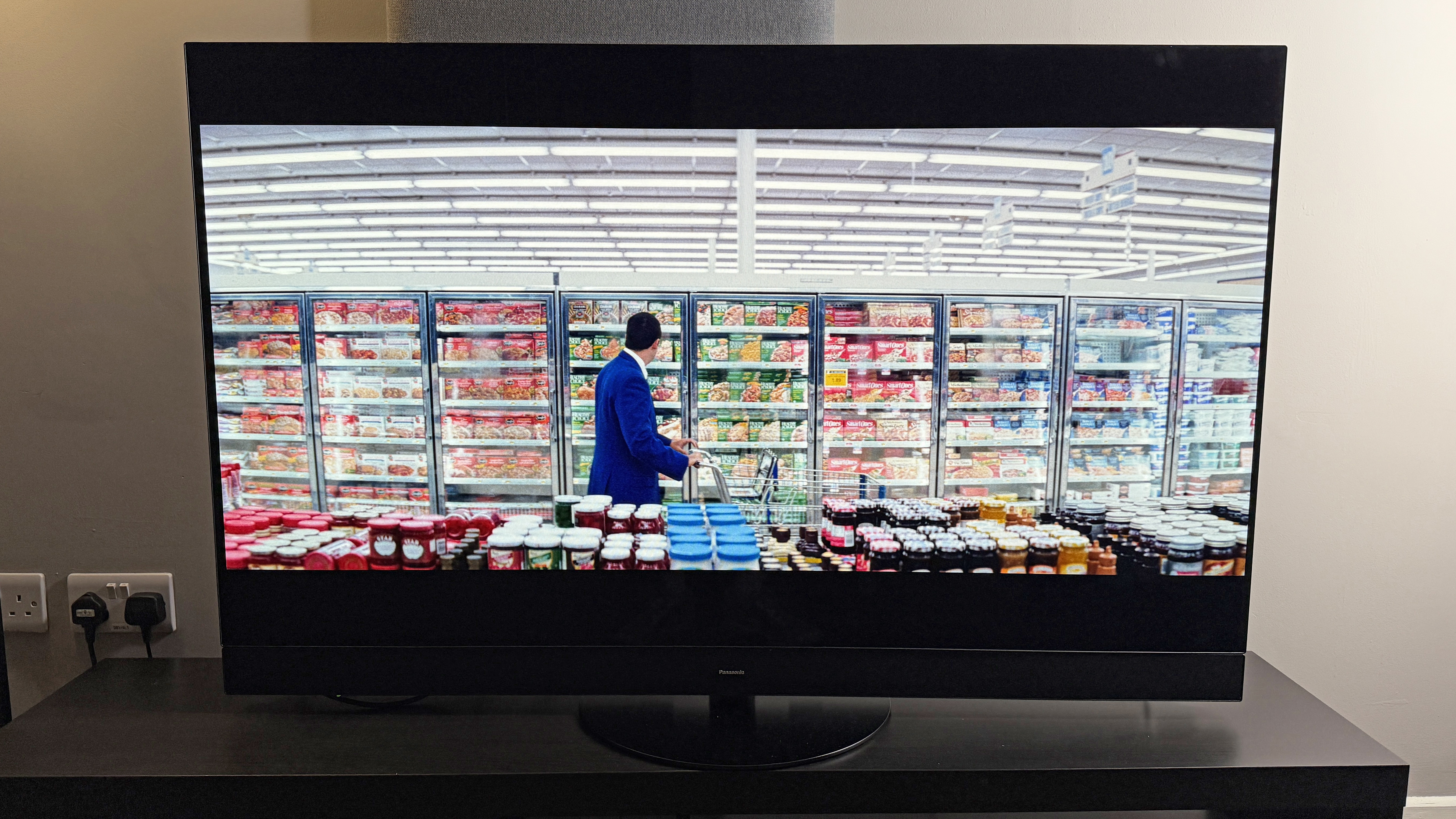 A TV showing the movie Punch-drunk Love. On-screen, Adam Sandler stands in front of a wide row of ready meals at a grocery store