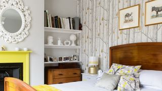 grey bedroom with woodland wallpaper on feature wall a yellow painted fire surround and alcove shelving to show how to organize a small bedroom efficiently