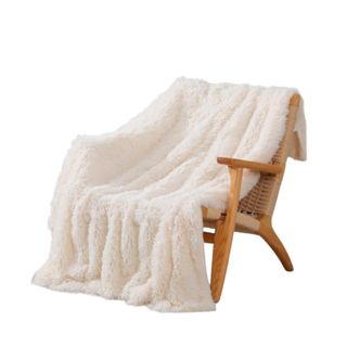 A white fuzzy throw blanket draped onto a light wooden armchair