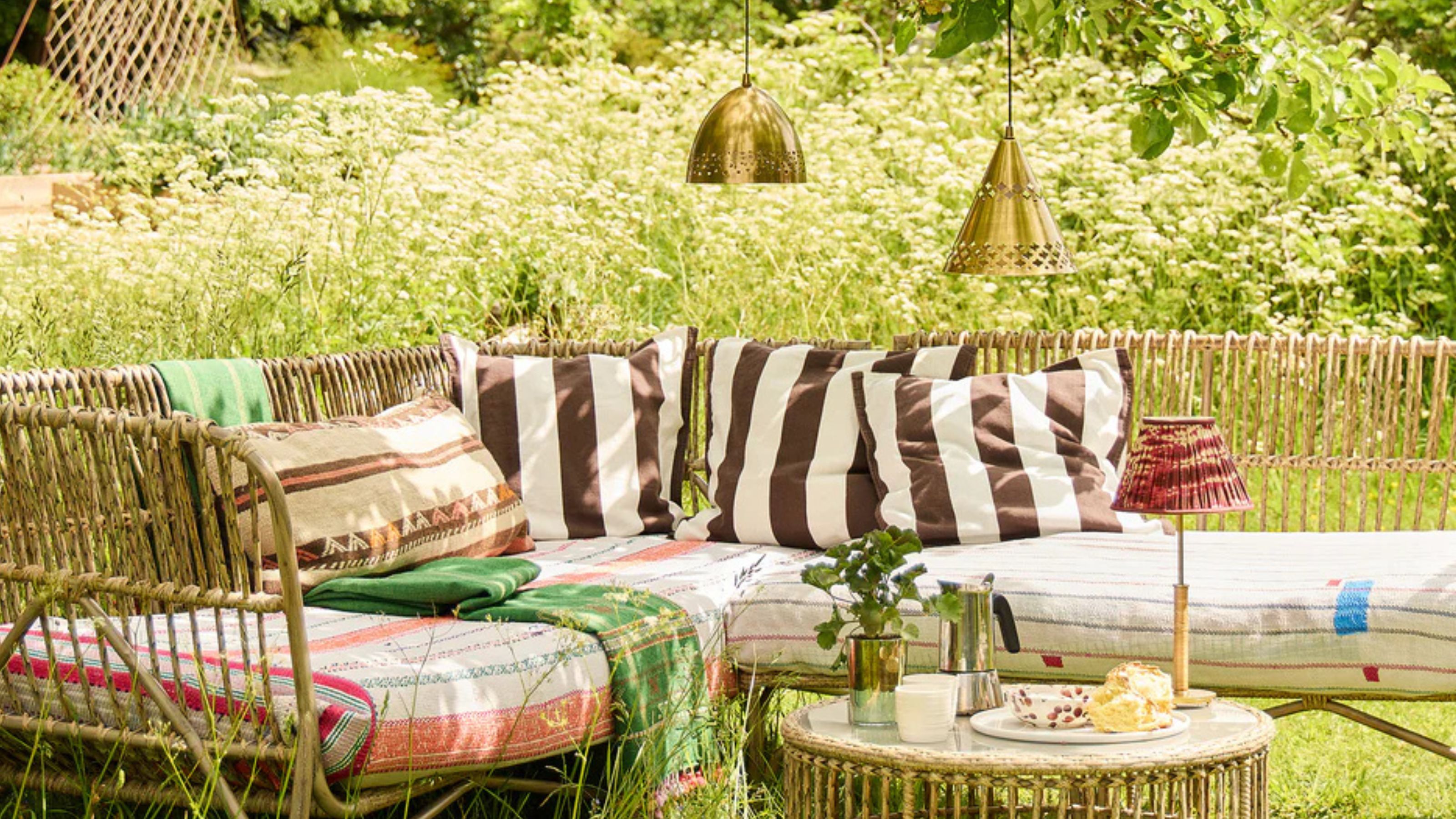 Pooky Brass Outdoor Pendant Lights hanging from a tree above a garden sofa and table set surrounded by greenery