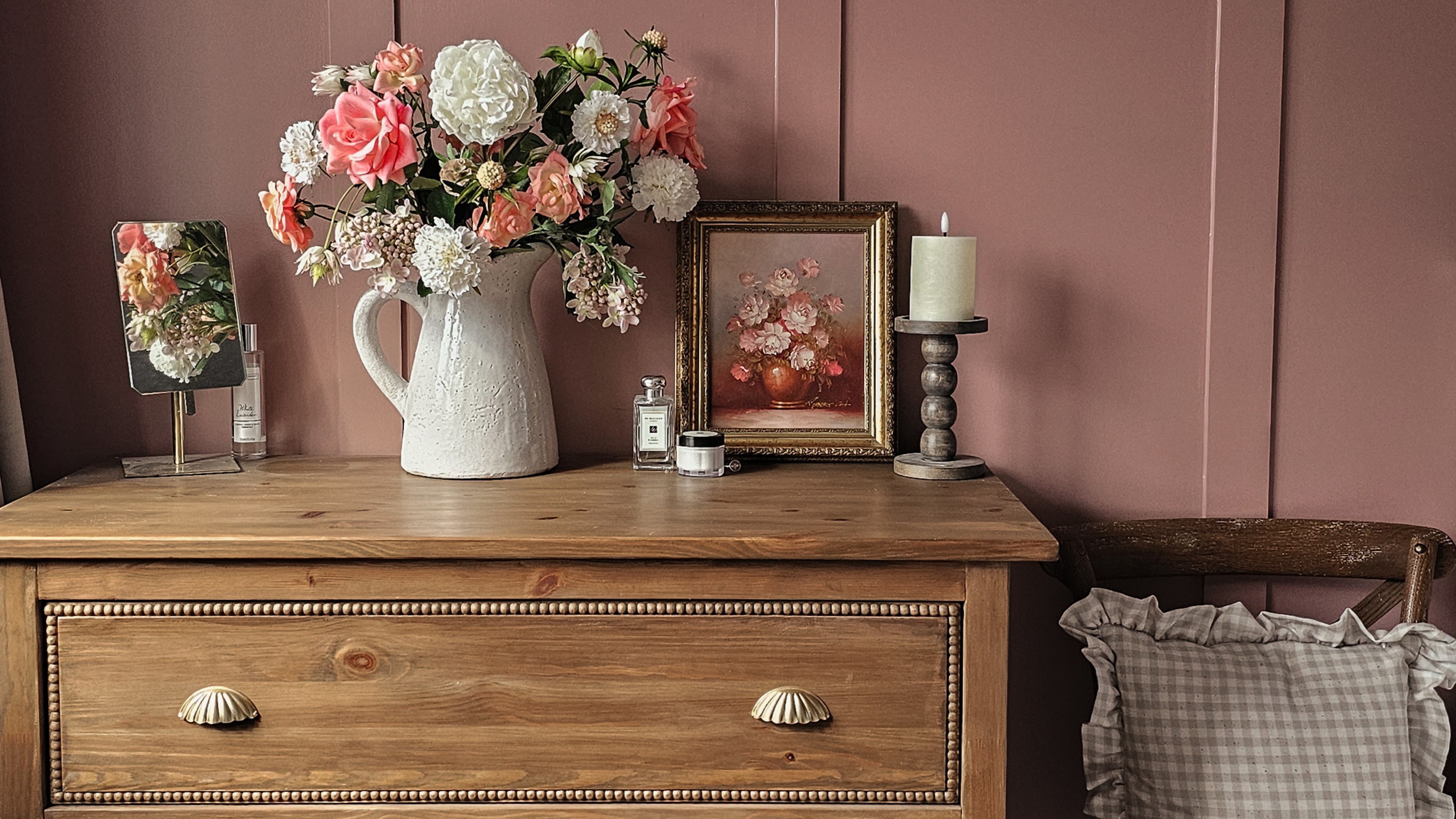 A vintage-style IKEA HEMNES dresser with a bobbin trim and scalloped handles and a jug filled with flowers on top set against a pink panelled wall