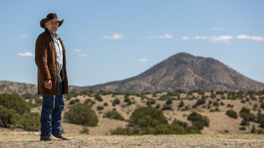 Walt Longmire wearing a cowboy hat and standing in a desert landscape looking at something off camera in Longmire.