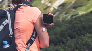 Active life of diabetics, woman hiking and checking glucose level with a remote sensor and mobile phone