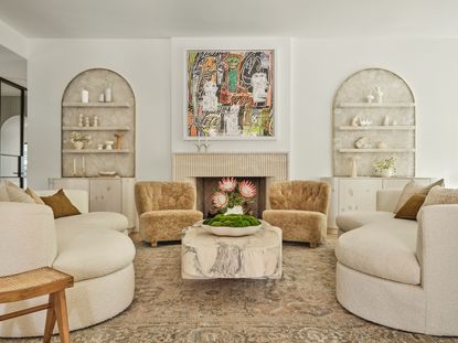 Living room with cream curved sofas, beige fluffy armchairs, pink stone coffee table and beige patterned rug