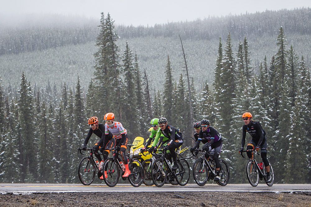 The day's breakaway riders ride through remnants of overnight snow on the sides of the roads