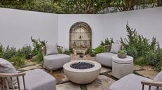 a walled spanish-style courtyard garden seating area with a stone water feature, stone flooring and firepit at the center