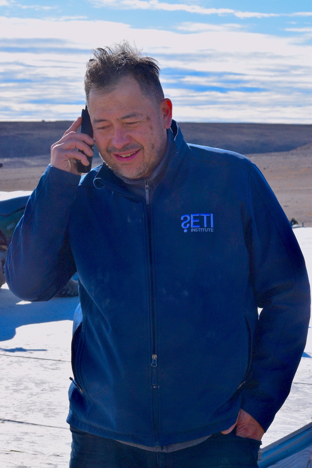 Pascal Lee in a blue sweater talking on a satellite phone.