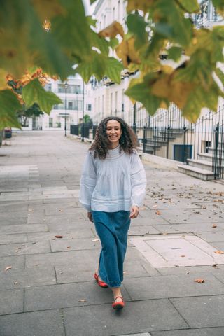 model wearing a pale blue blouse, jeans and red ballet pumps