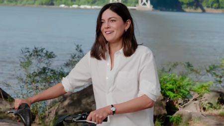 Monica Barbaro smiling while holding on to bike handles in One Night Only. 