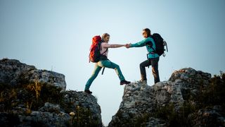 Woman helping friend across gap in the rocks on hiking trip