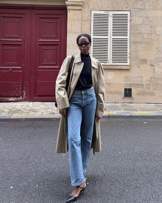 Sylvie wears a trench coat, blue jeans and slingbacks