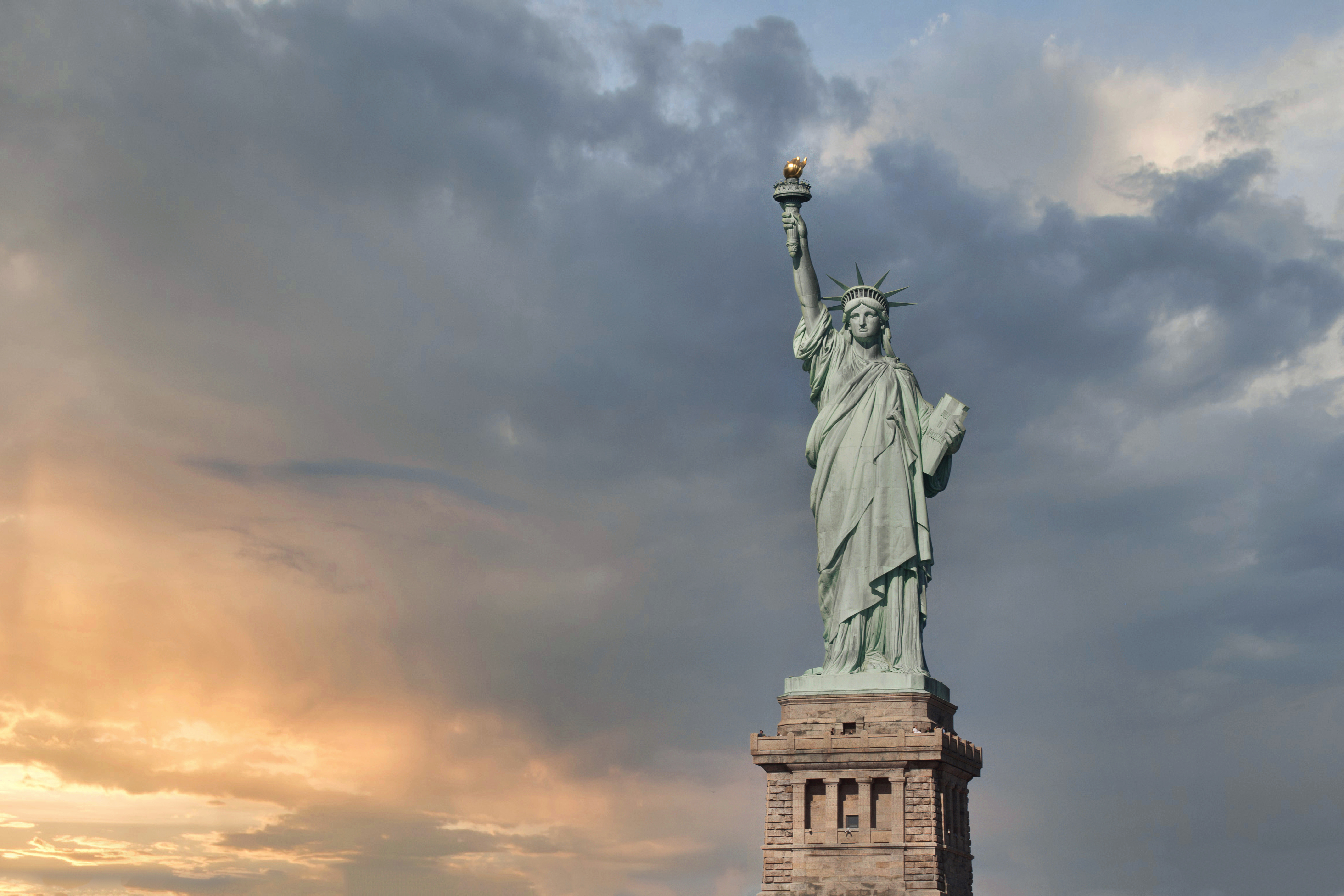 The Statue of Liberty, viewed from below, with a cloudy, sunset sky in the background