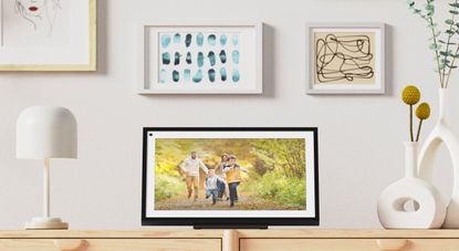 An Amazon Echo Show 15 on a wooden side cabinet displaying a family photo