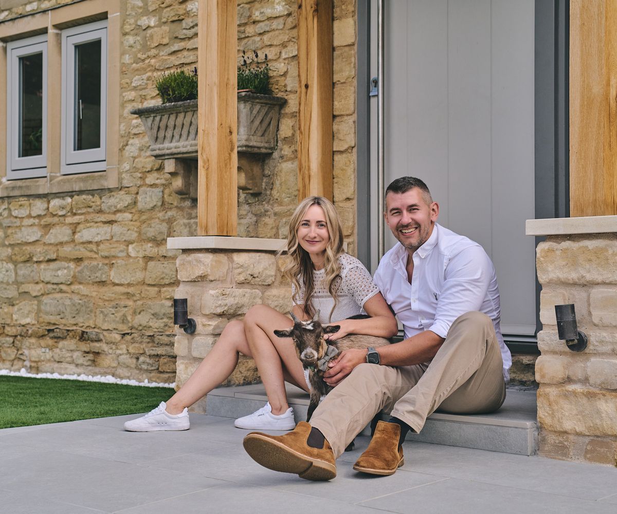 Couple sitting on the step in front of their door with a pet goat