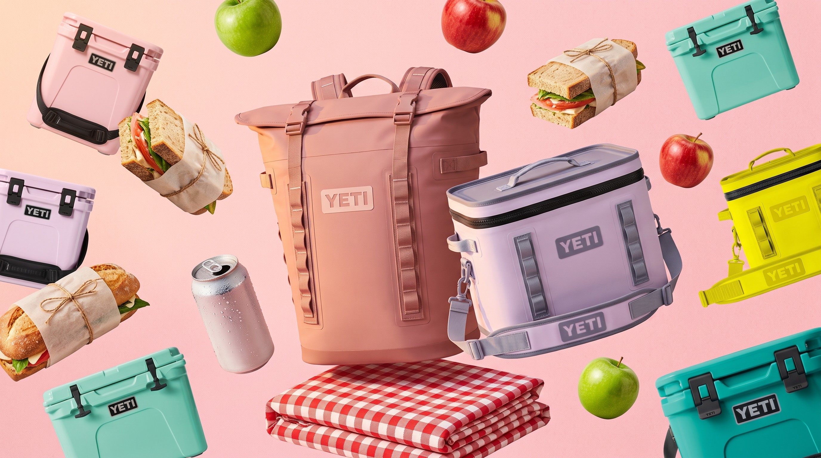 Collection of hard and soft Yeti coolers on a pink background with a picnic blanket, apples, and sandwiches