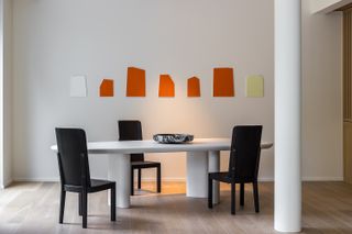 a white dining table with black chairs and orange artworks