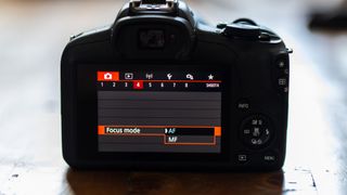 The menu on the rear LCD screen of a Canon EOS R100 showing how to switch between MF and AF focus