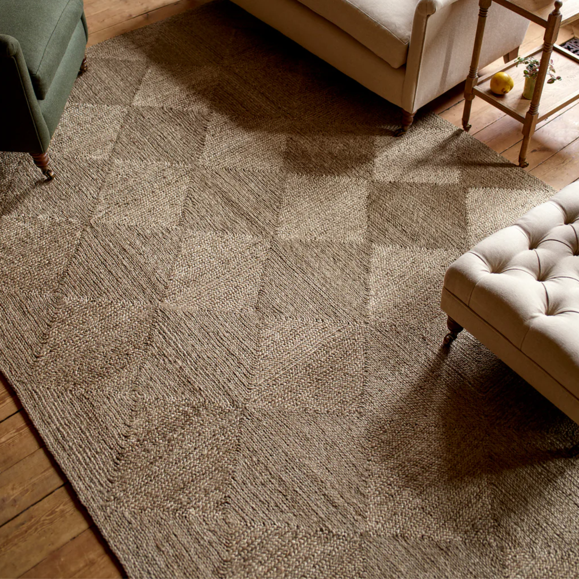 a large jute area rug that is woven to create a diamond motif. On top of the rug are pieces of furniture including a chair, a couch, and a tufted ottoman