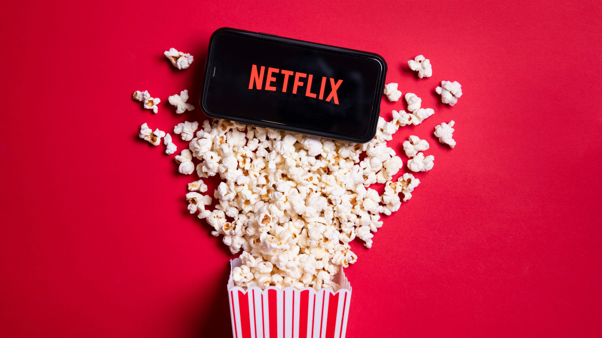 Netflix op een smartphone op een omgegooide beker met popcorn