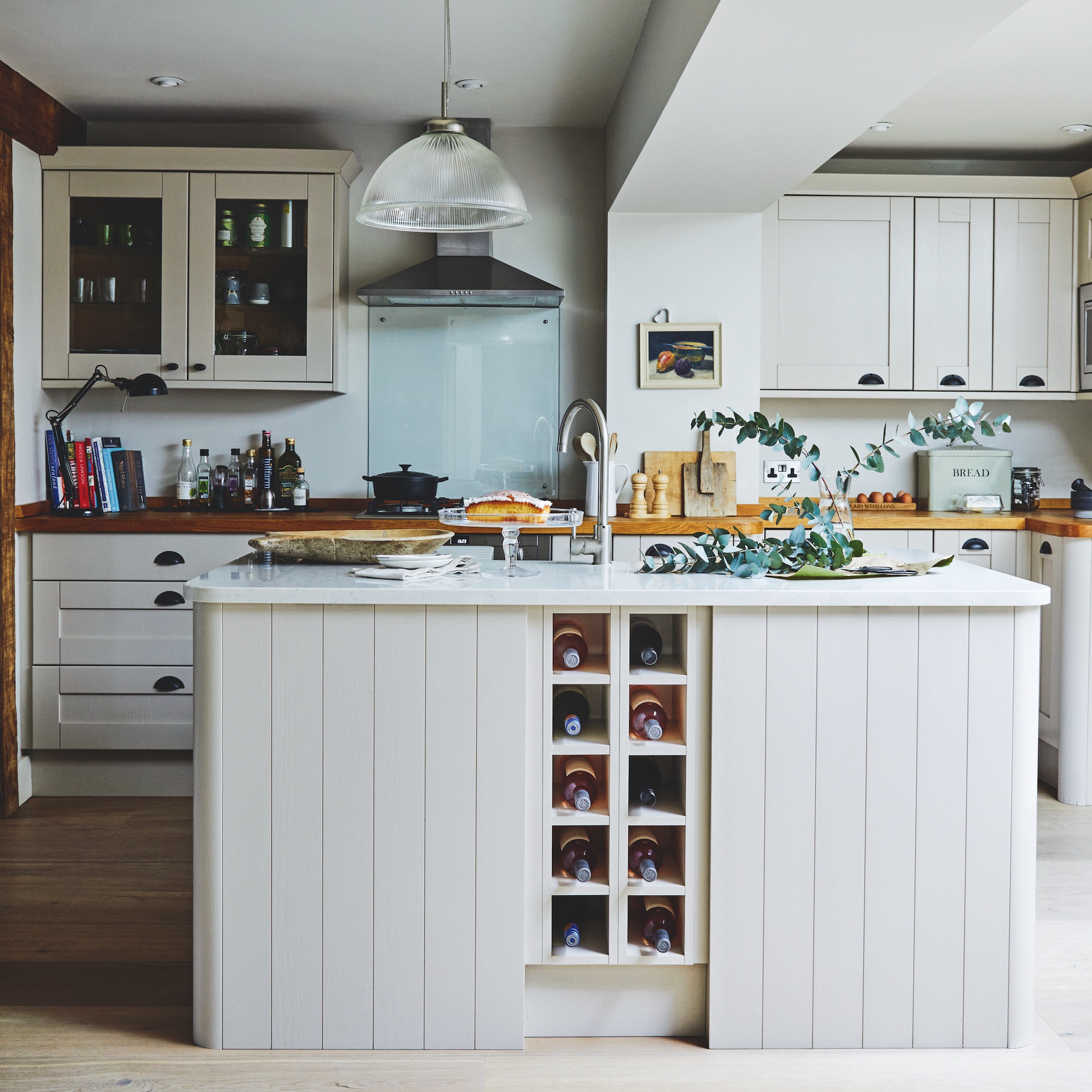 cottage kitchen with square island with wine racks and sink with tap, with farmhouse style cabinets behind in white