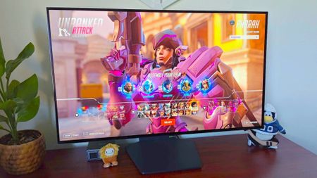 LG UltraGear 32GS95UE-B gaming monitor with Pharah from Overwatch 2 on screen on woodgrain desk