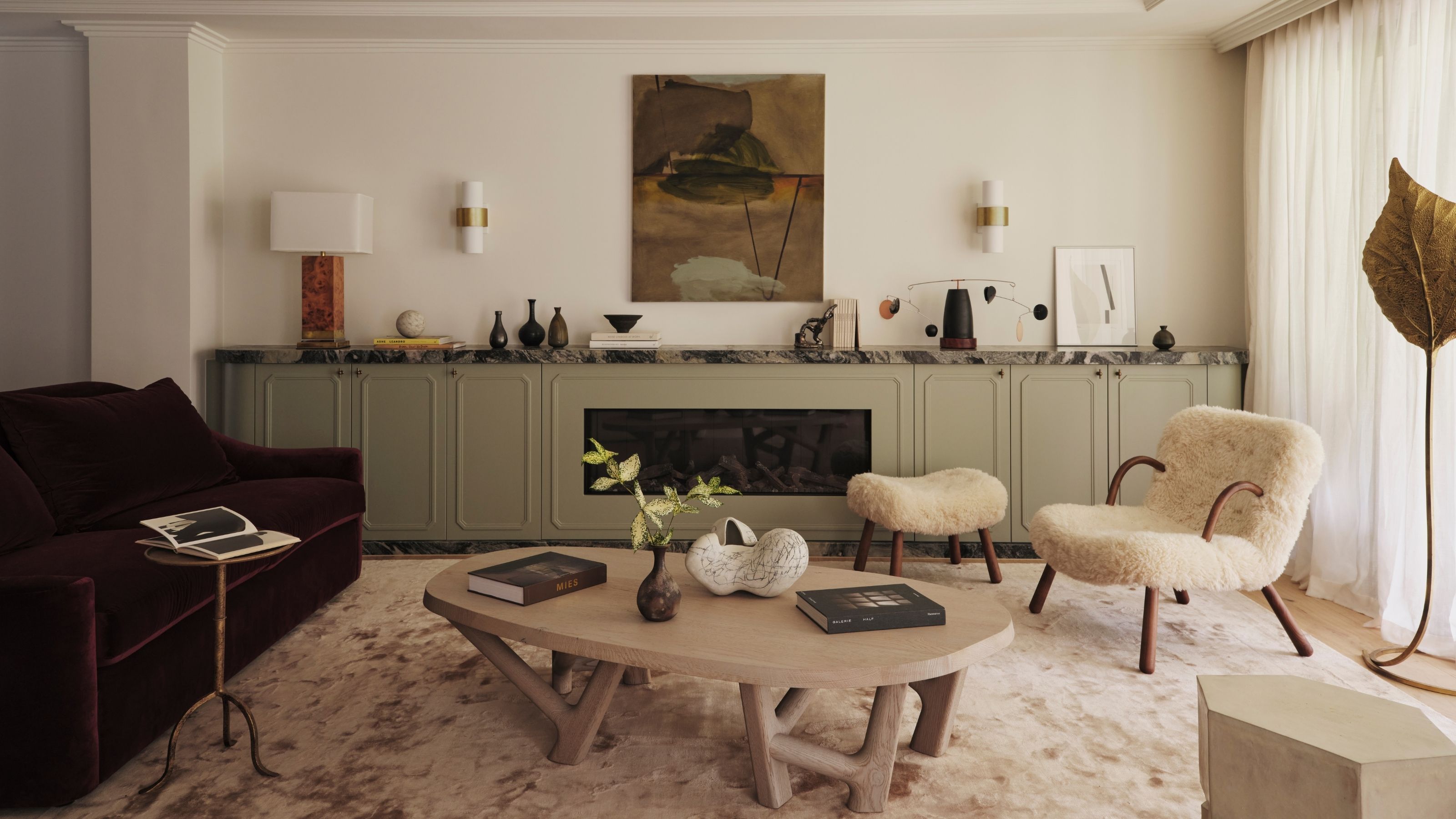 Image of a white living room with lots of light. A sage green console across the back wall with decor on it, a purple sofa, a neutral rug, and a light wood coffee table.