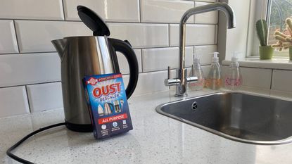 An electric kettle with Oust descaling solution in white tiled kitchen 