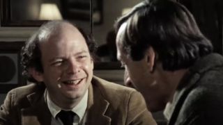 Wallace Shawn smiling, sitting across from Andre Gregory in My Dinner with Andre