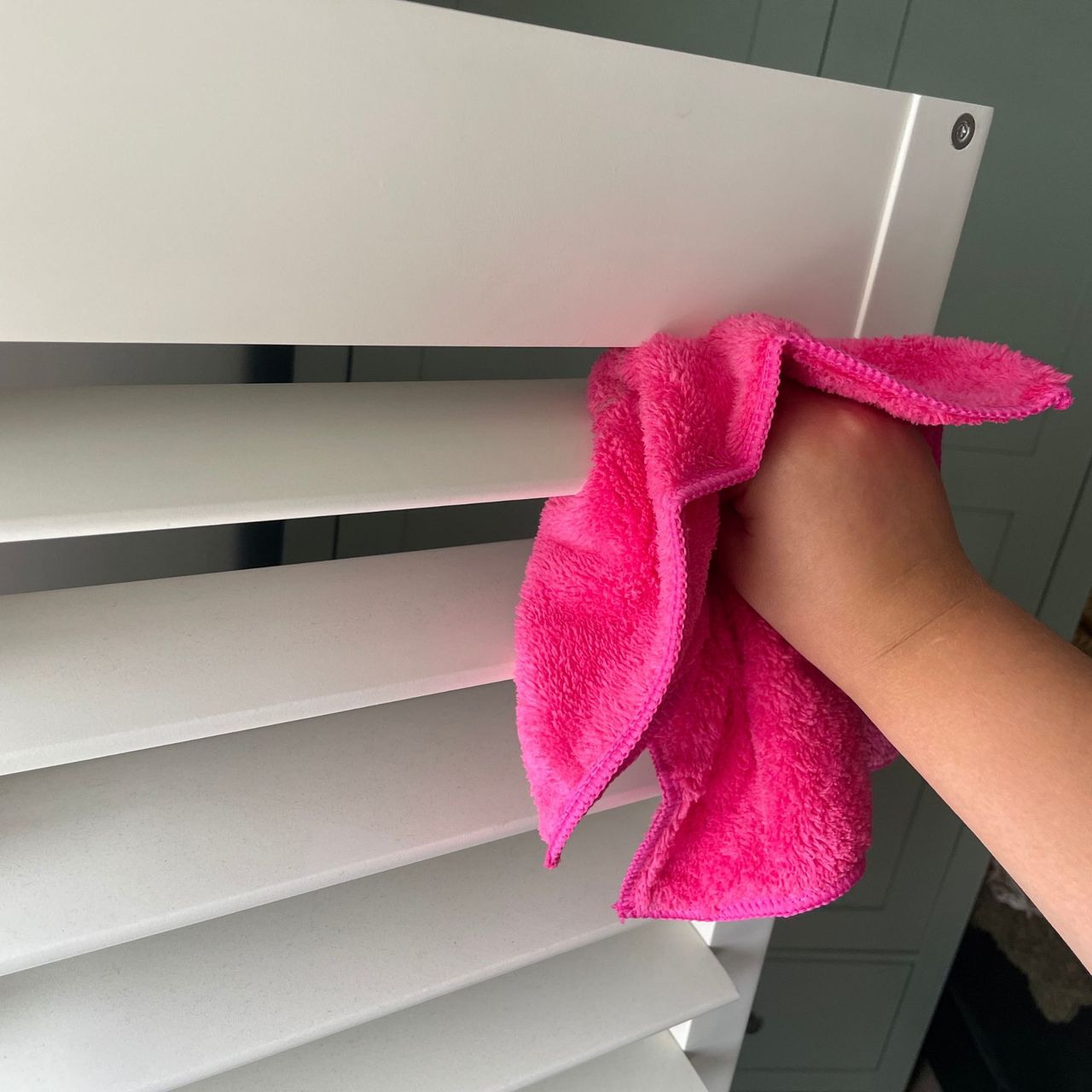 Using a pink Minky Cloth duster to dust upper slat of plantation shutters