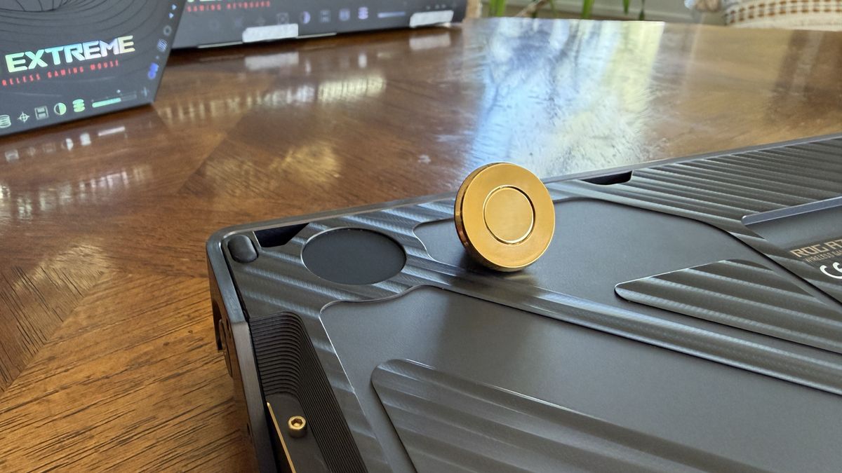 Close-up of a dark gray ASUS ROG Azoth Extreme Edition 20 with a gold circular object on a wooden surface, and a box labeled "EXTREME" in the background.