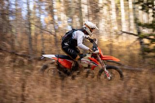 A motocross rider riding through a wooded scene