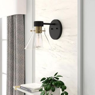 A black, glass and brass wall sconce on a bathroom wall