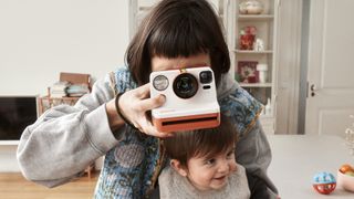 Mother holding a Polaroid Now 3 instant camera and child