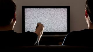 Two men sit in front of a TV set with static on the screen.