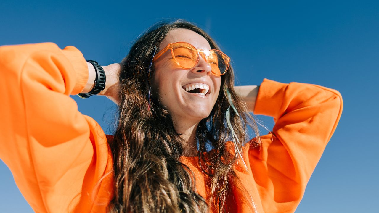 best vitamin c moisturisers - woman with glowy skin in bright orange jumper and sunglasses - getty 2181139566