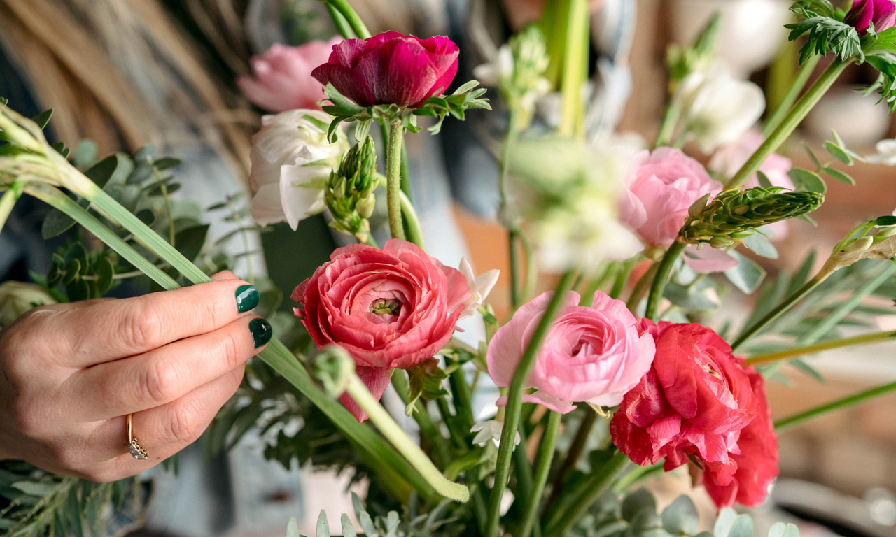 Hand placing narcissi into a vase of ranunculus and other flowers
