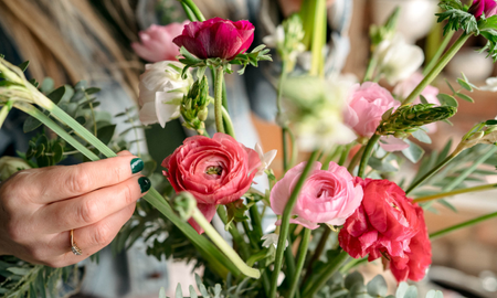 Hand placing narcissi into a vase of ranunculus and other flowers