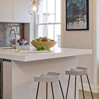 White kitchen island with swivel tap and zinc with a bowl of fruit on top and 2 chairs next to it