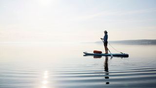 Woman on stand-up paddleboard across clear lake in the sun