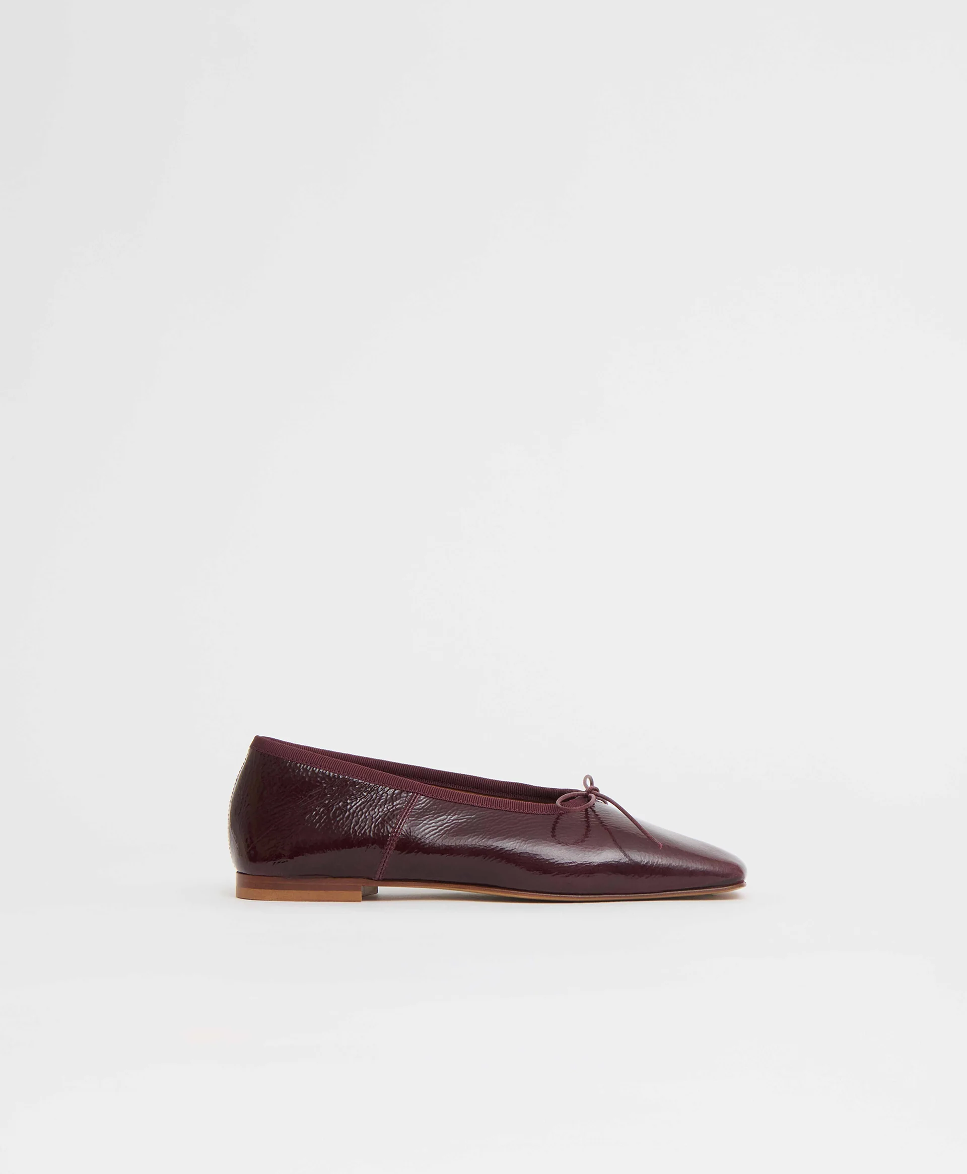 A dark oxblood ballerina featuring a knotted bow, grosgrain trim, and a low stacked heel.