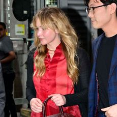 Jennifer Lawrence in NYC wearing a red top, black lace-trim skirt, flats, and carrying her The Row lady bag.