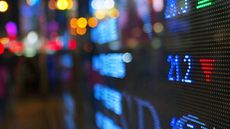 A stock market ticker board shows a stock heading lower