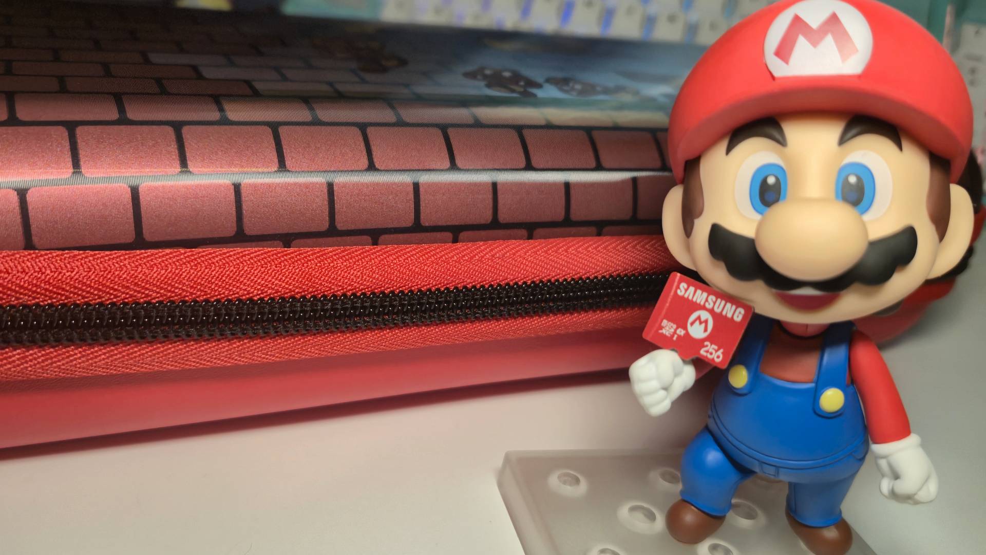 Photo of a Mario nendoroid figure holding a microSD Express card with a Turtle Beach Switch 2 case in the background.