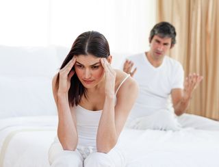 frustrated woman with headache sitting on a bed with partner