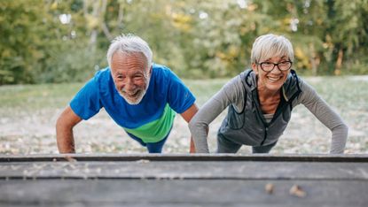 Smiling woman and man performing push-ups with their hands on the seat of a bench