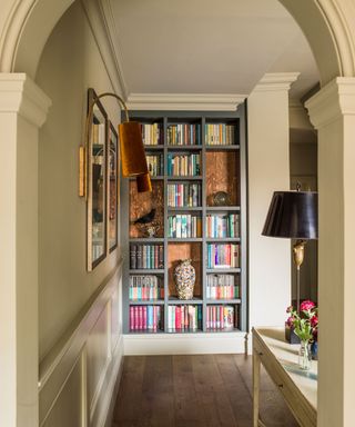 Narrow hallway with gray painted bookcase and architectural arch features.