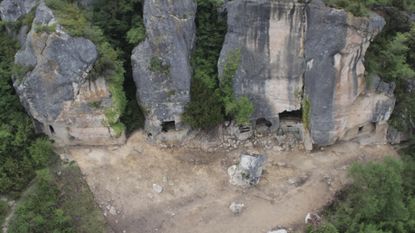 An aerial photo of a tall cliff wall with cave openings on the bottom
