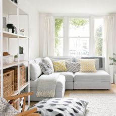 Grey corner sofa in white living room with floor to ceiling windows and shelves