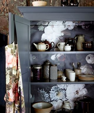 Close up of dark gray pantry shelving with a moody dark floral wallpaper behind.